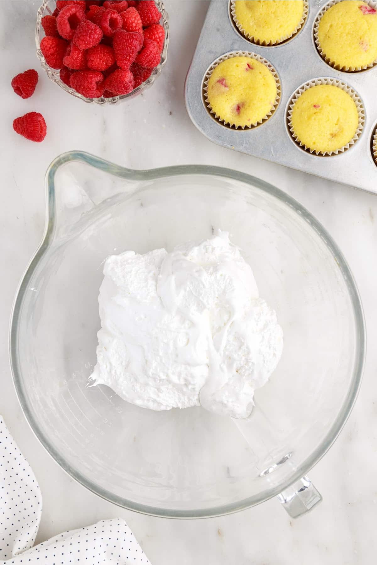 Marshmallow cream in a bowl next to cupcakes and raspberries.