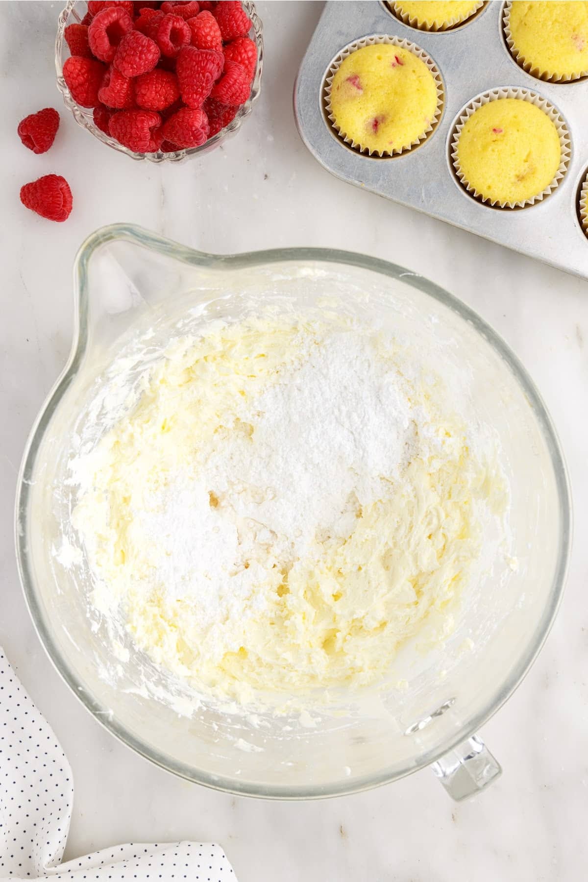 Flour added to the marshmallow cream mixture next to a dish of raspberries and cupcakes.