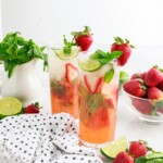 Two Strawberry Mojitos with a bowl of mint and strawberries.