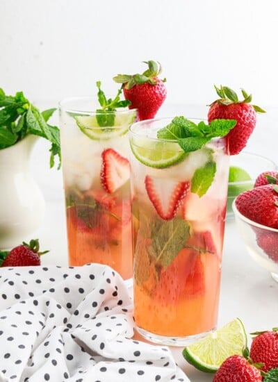 Two Strawberry Mojitos with a bowl of mint and strawberries.