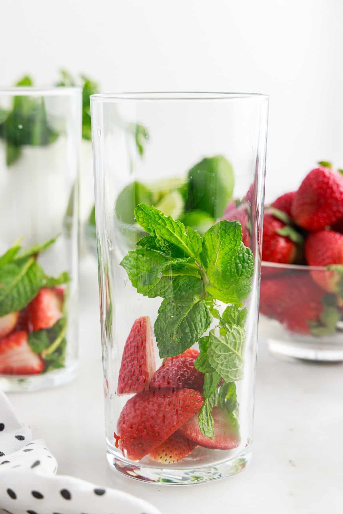 A tall glass with strawberries and mint in it.