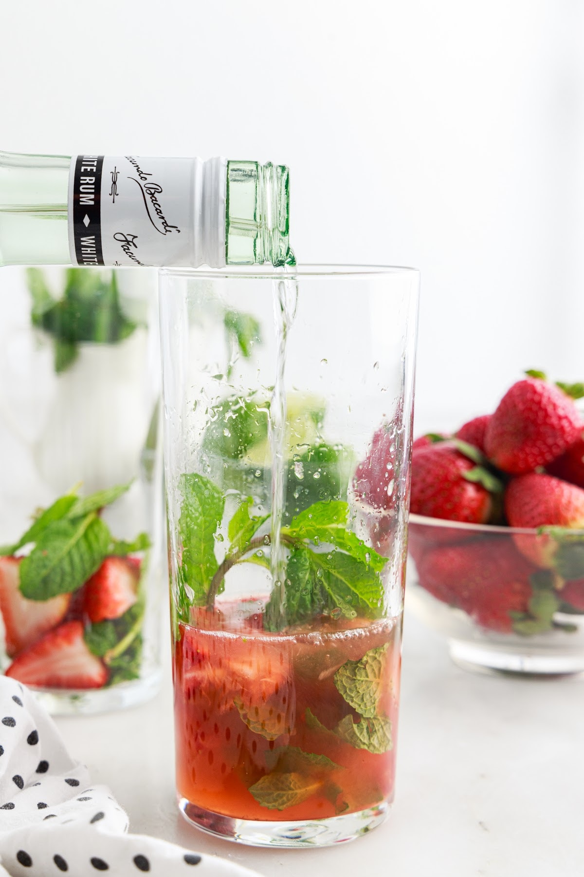 Rum added to ingredients in a tall glass to make a Strawberry Mojito.