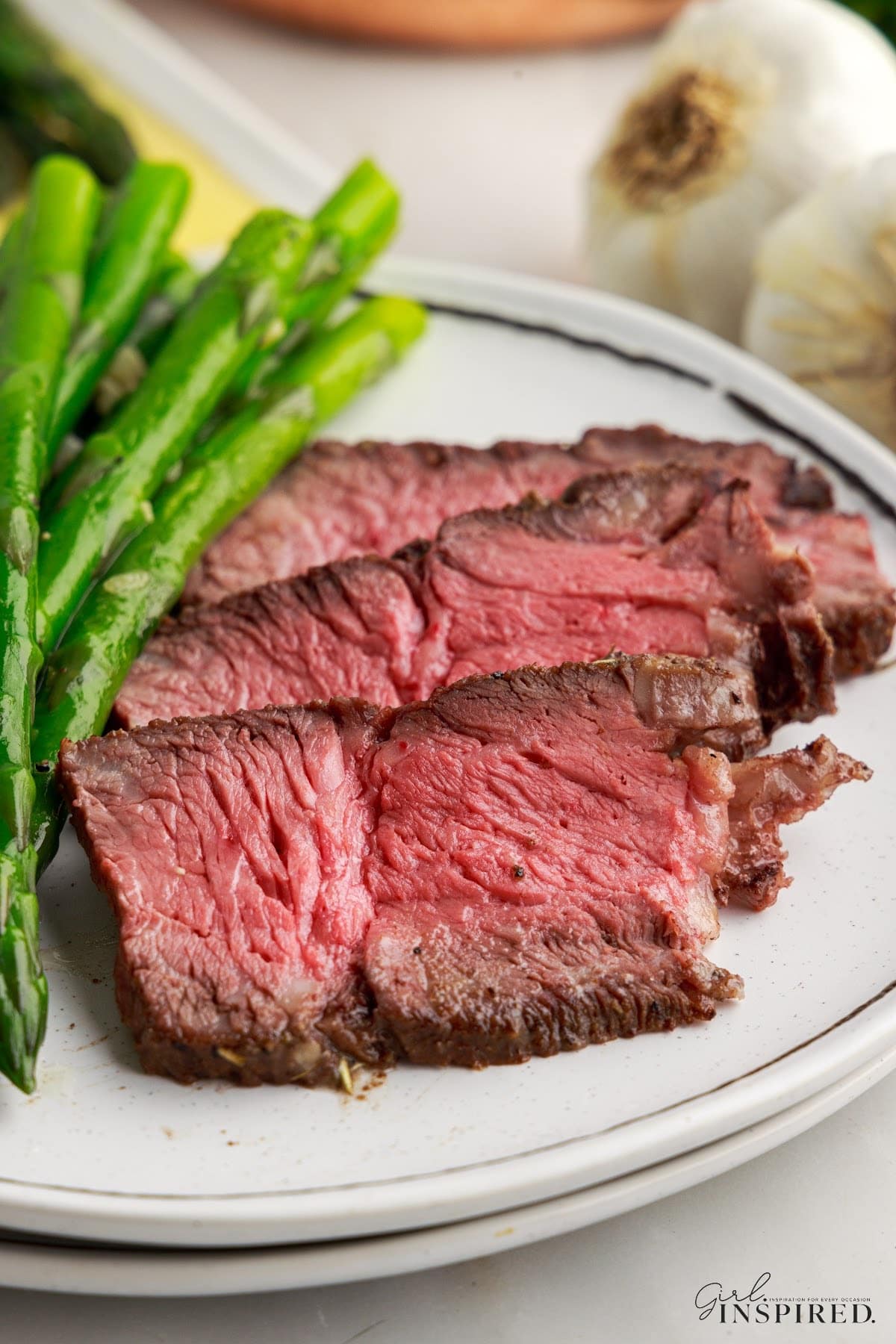 Slices of Air Fryer Roast Beef on a plate with asparagus.