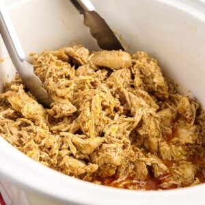 Close up of shredded chicken in a crockpot with tongs.