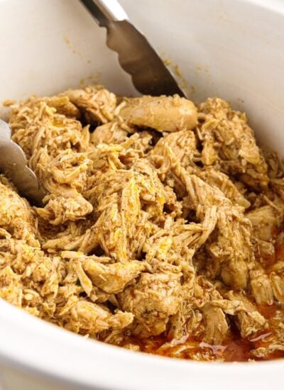 Close up of shredded chicken in a crockpot with tongs.