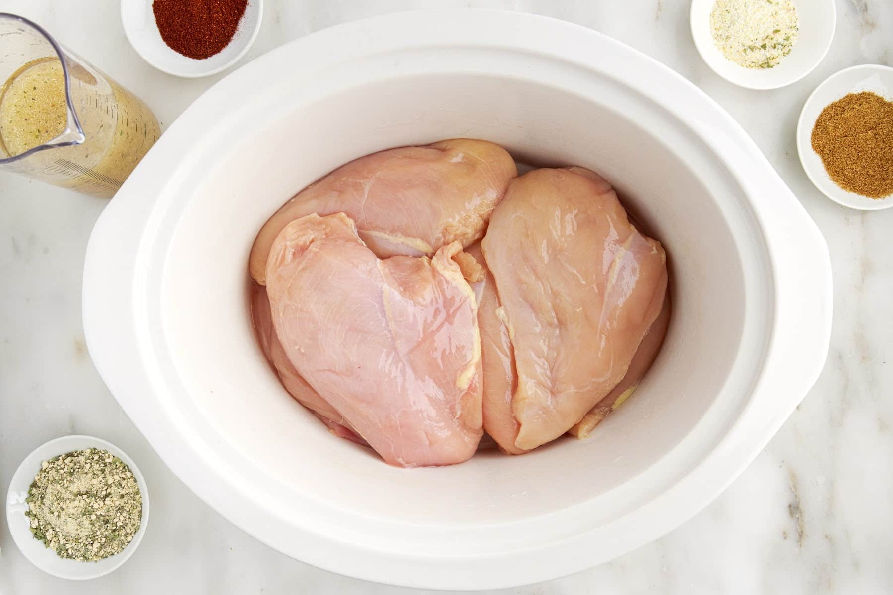 Chicken breasts in a crockpot before cooking spices surrounding crockpot.
