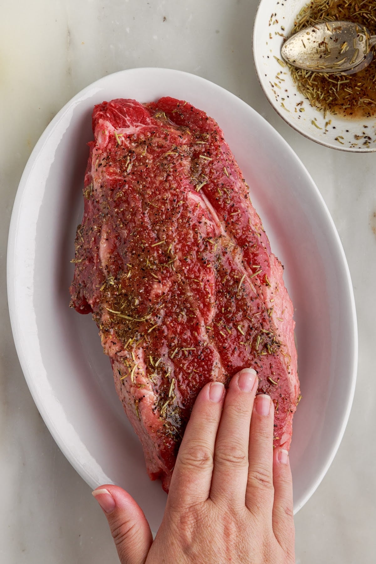 Roast beef with seasonings spread on it in an oval dish.