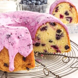 Front view of a Blueberry Pound Cake with slices missing and a slice on a dish in the background.