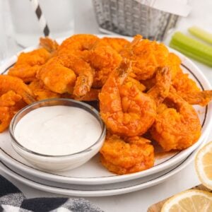 A plate full of Buffalo Shrimp next to sauce.