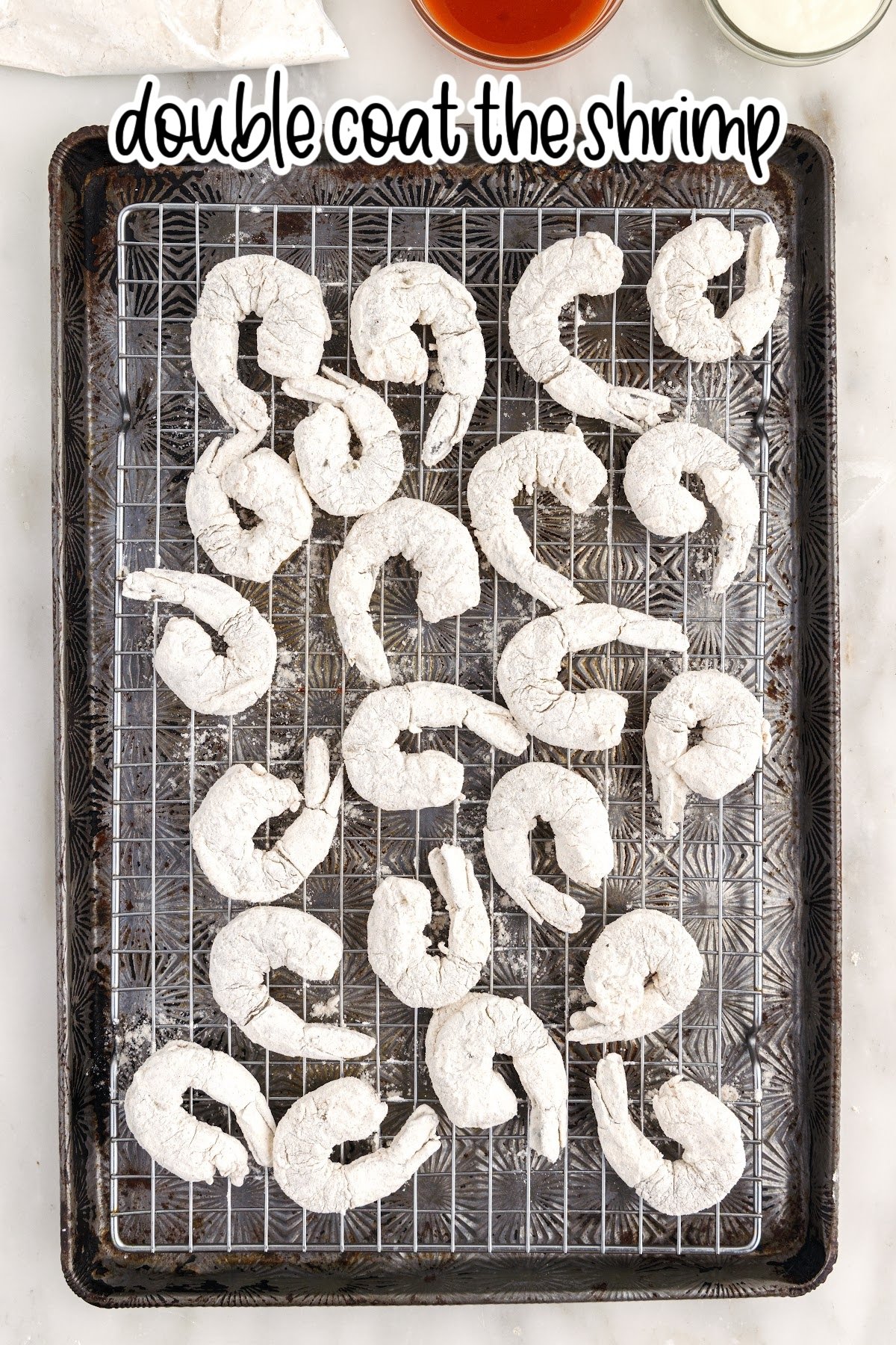 Buffalo Shrimp on a rack on a cookie sheet after being breaded with text overlay.