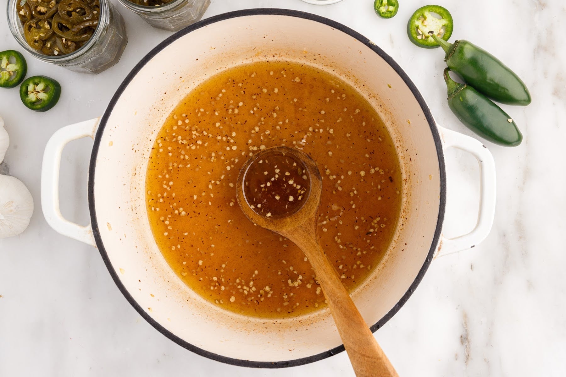 Candied Jalapeños liquid in a dutch oven with a wooden ladle.