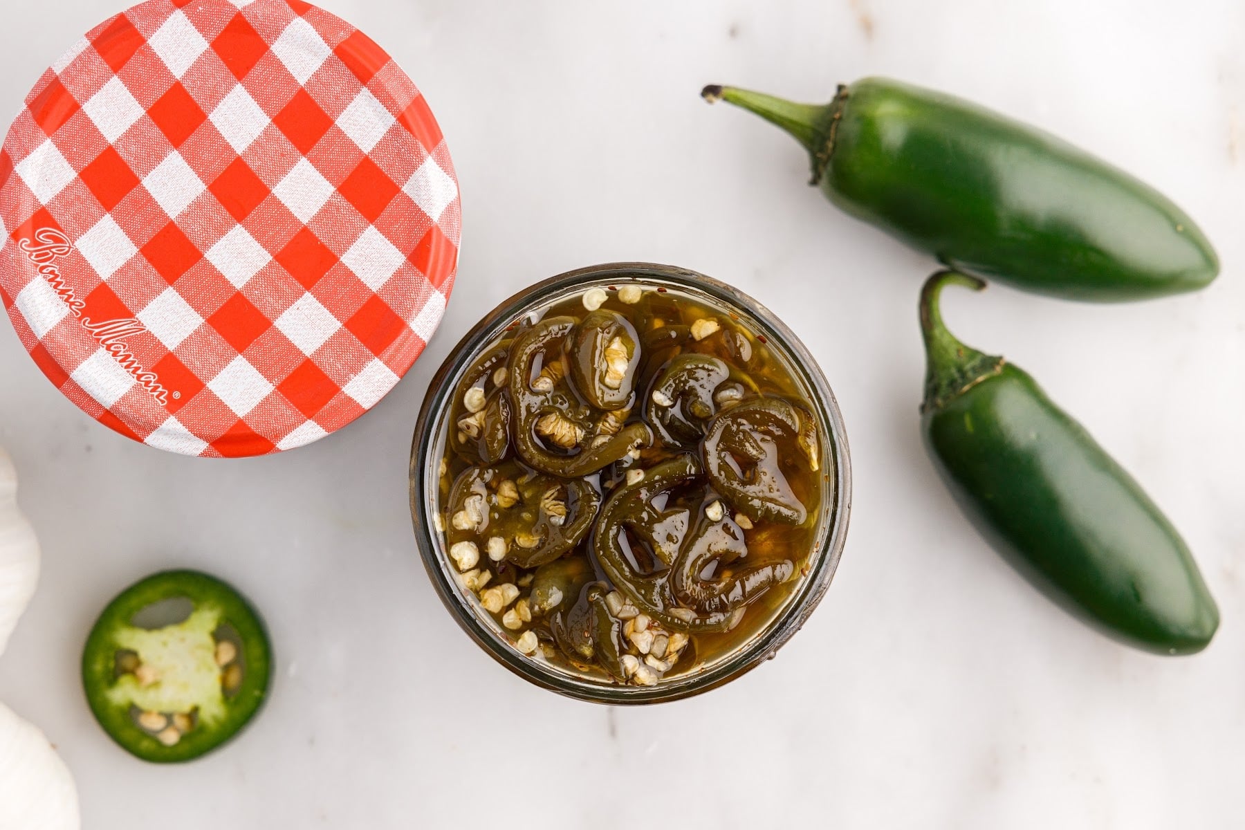 Candied Jalapeños in a canning jar next to jalapenos.