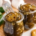 Close up of two jars of Candied Jalapeños with a fork inserted.