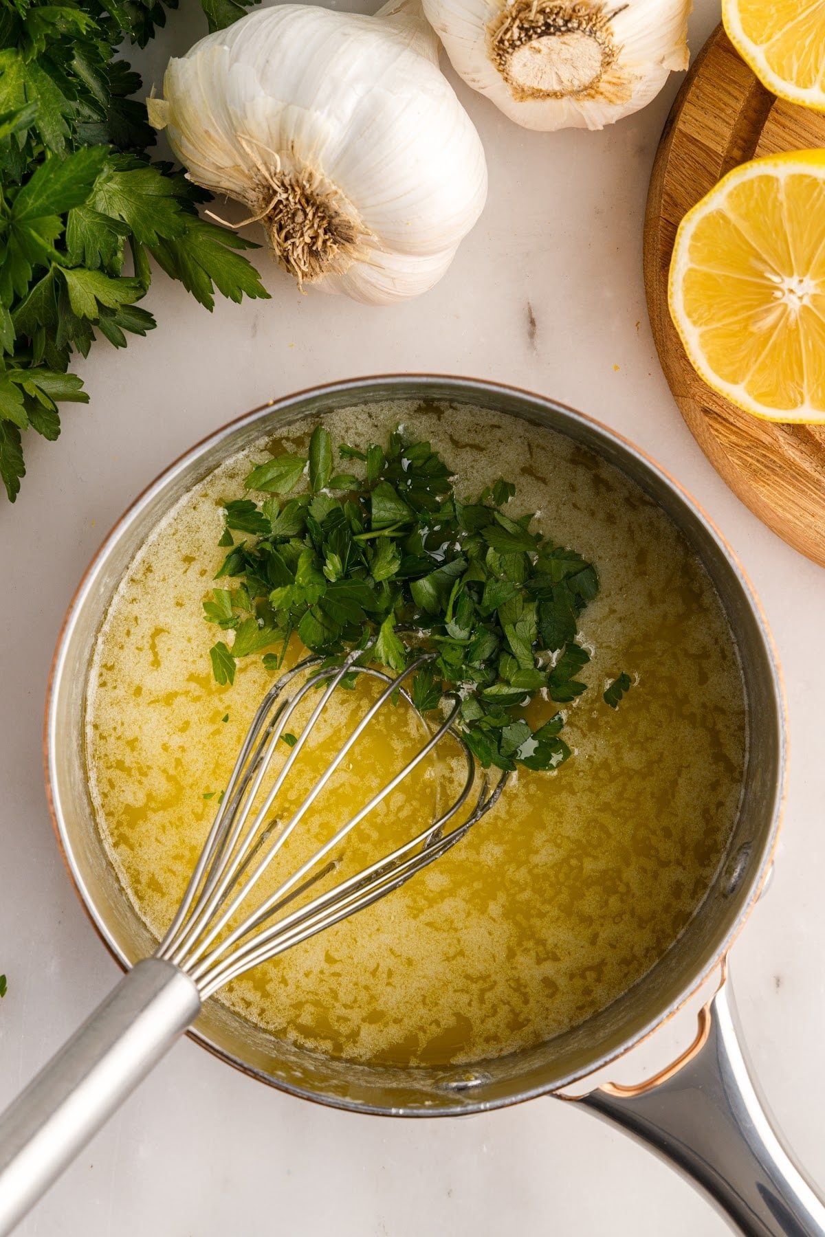 Chopped parsley added to Garlic Butter Sauce in a sauce pan with a whisk inserted.