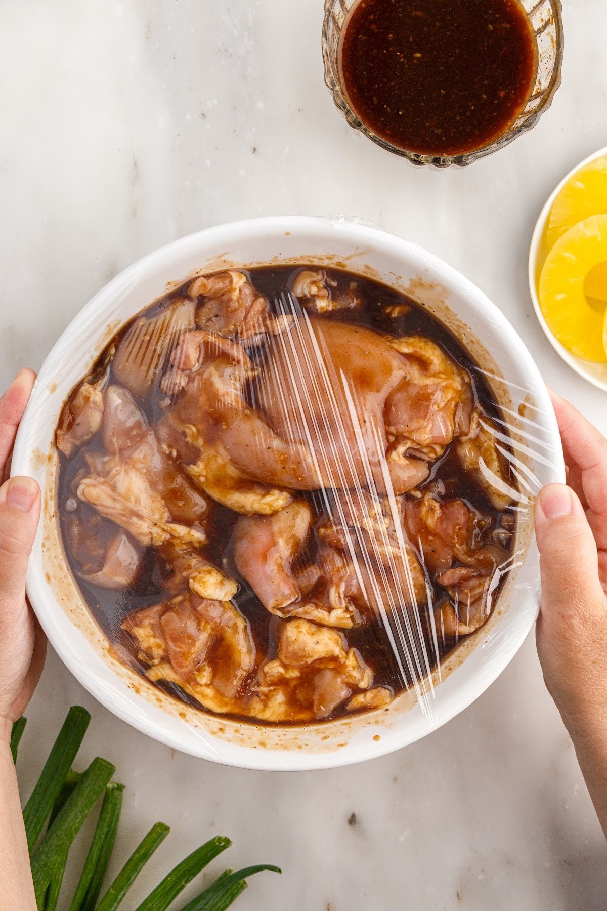 Huli Huli Chicken in a bowl of marinade with saran wrap placed on top.