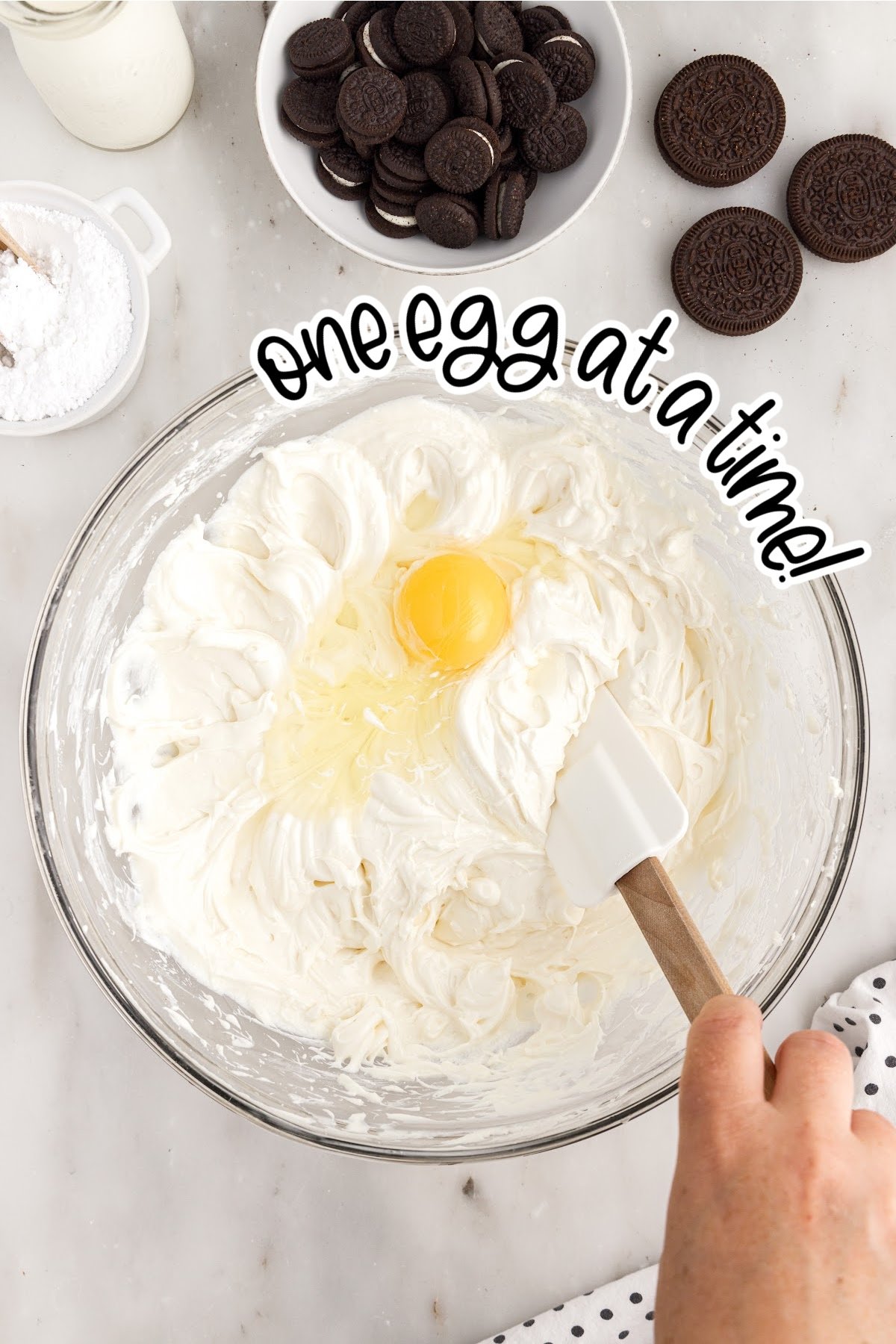 Egg added to the cream cheese mixture in a mixing bowl with text overlay.