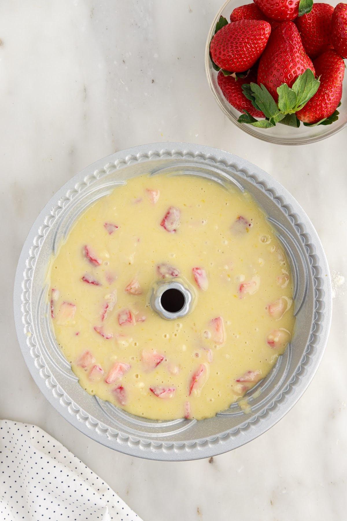 Strawberry Bundt Cake batter added to a bundt pan next to a bowl of strawberries.