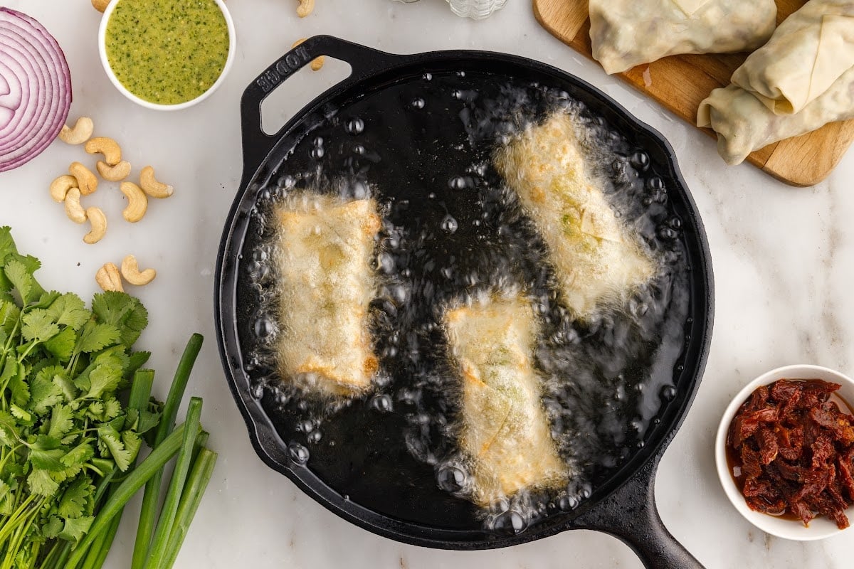 Three Cheesecake Factory Avocado Egg Rolls in a skillet of oil.