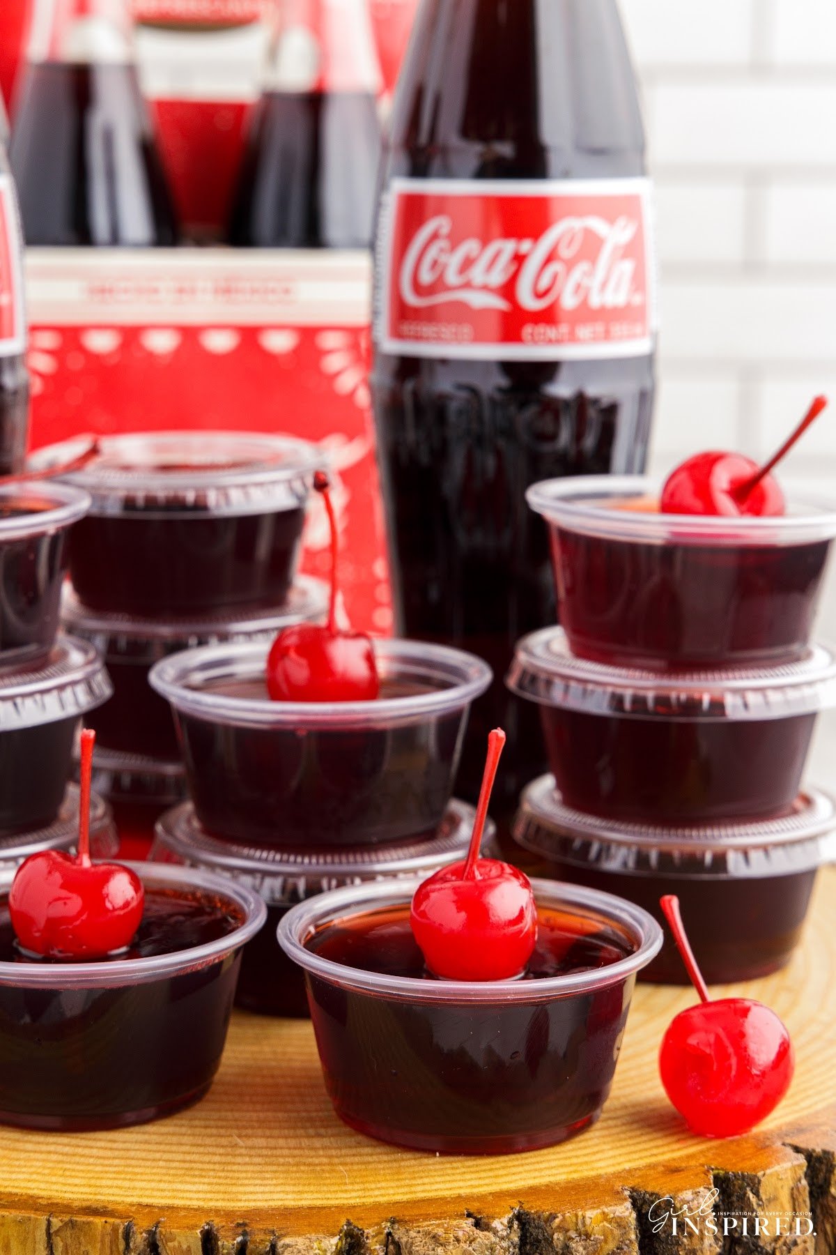 Front view of stacked Cherry Coke Jello Shots with a Coca-Cola in the background.
