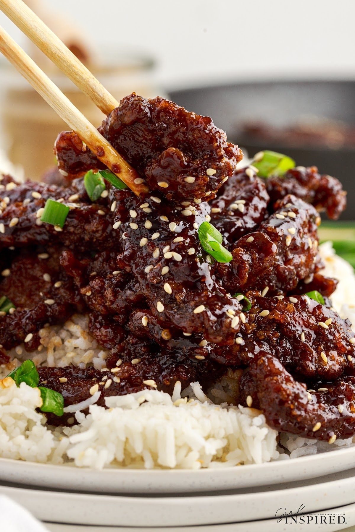 Front close up of Ginger Beef over rice on a plate with chop sticks.