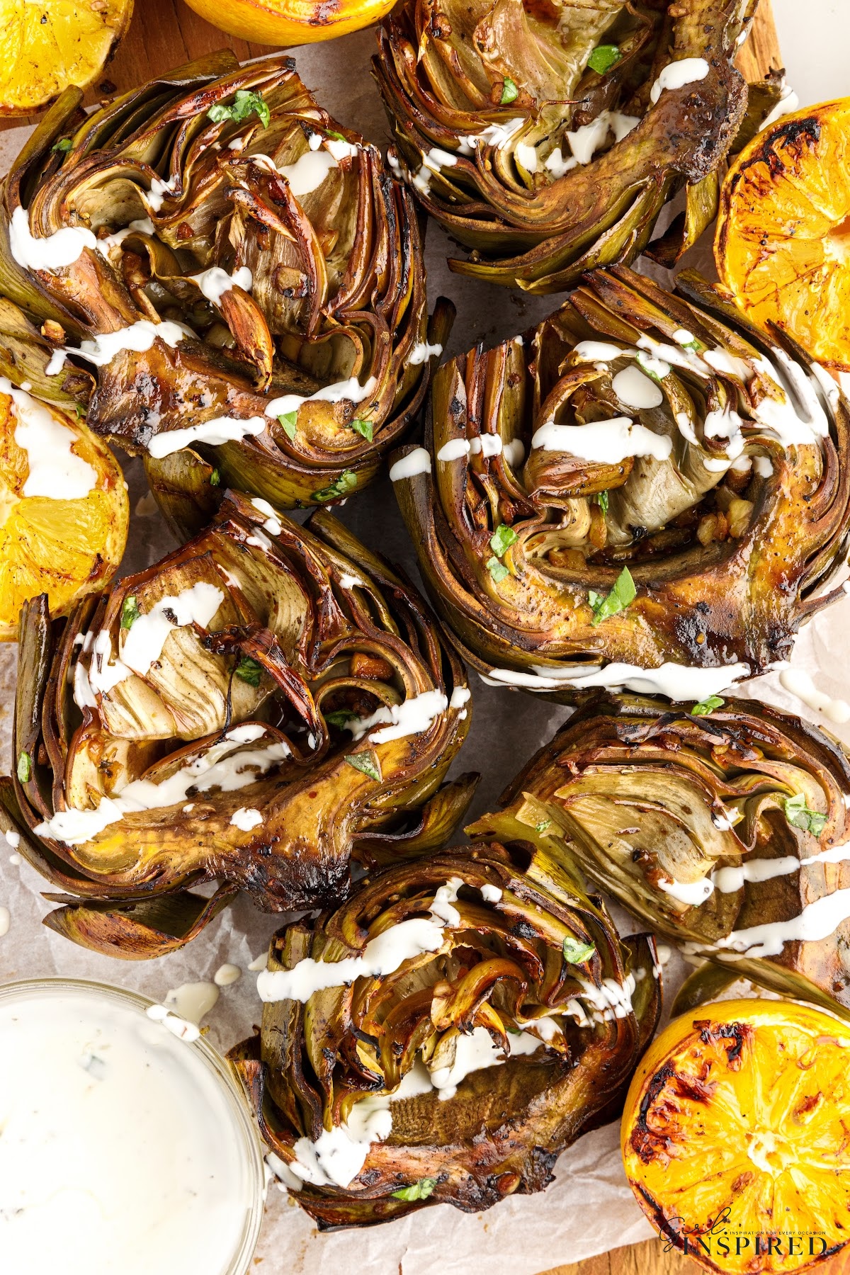 Overhead view of Grilled Artichokes next to lemon wedges and dipping sauce.