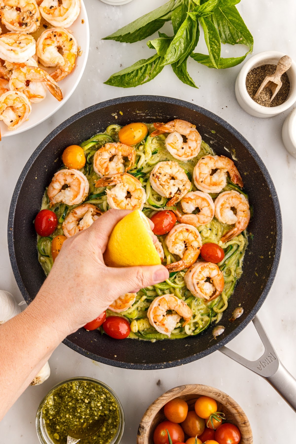 Lemon squeezed on Pesto Zucchini Noodles with Shrimp in a skillet.