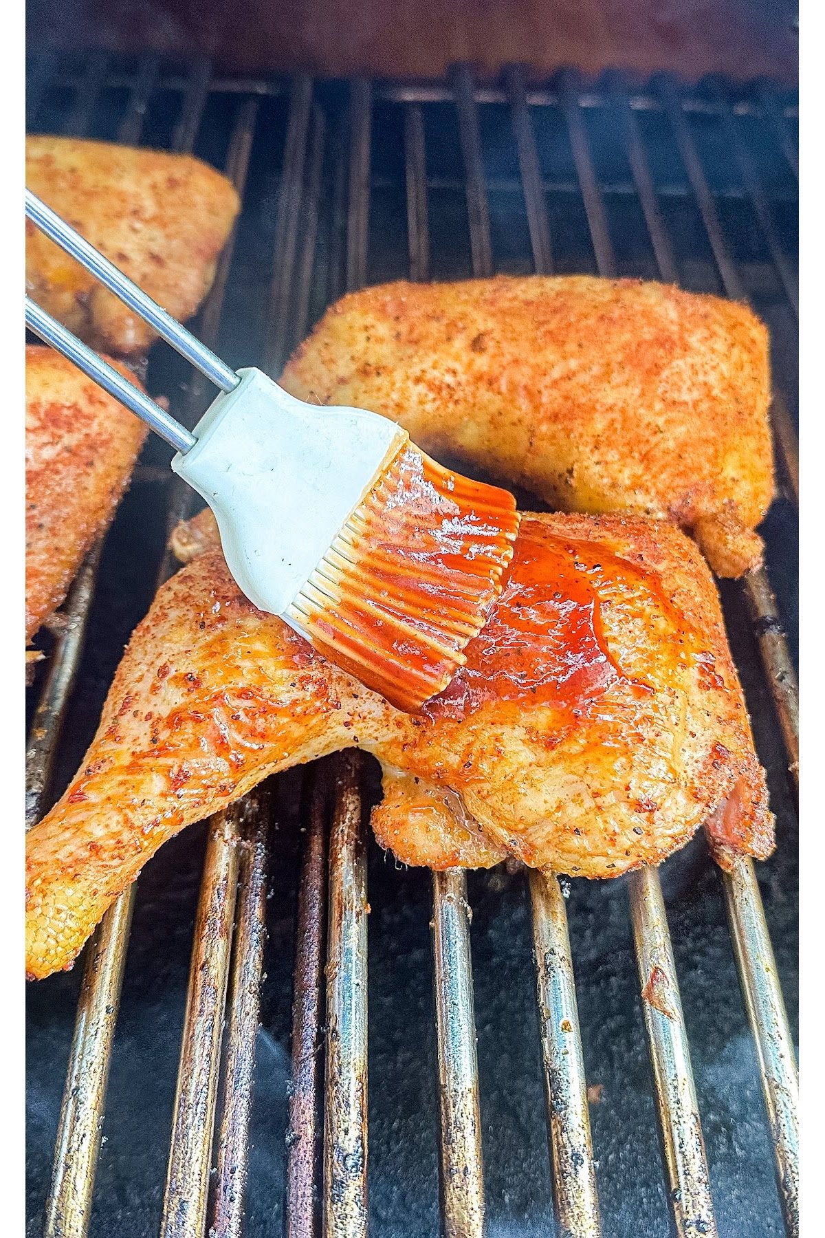 Chicken leg quarters being brushed with BBQ sauce on the grill.