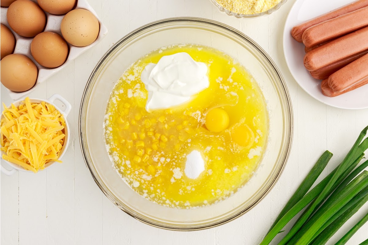 A mixing bowl of cream style corn, sugar, melted butter, sour cream, and eggs.