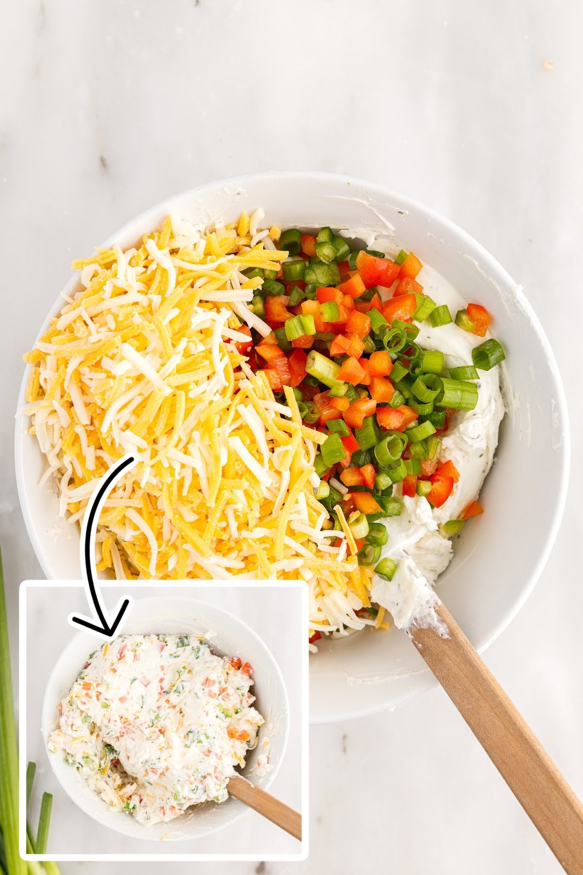 Mixing the cream cheese, veggies, and other cheese in a white mixing bowl.