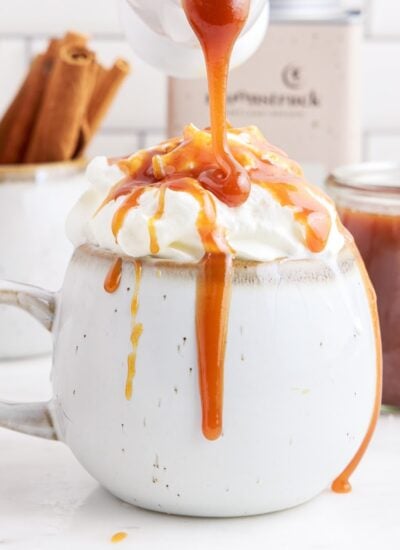 Starbucks Dark Caramel Sauce drizzled on a drink in a mug topped with whipped cream.