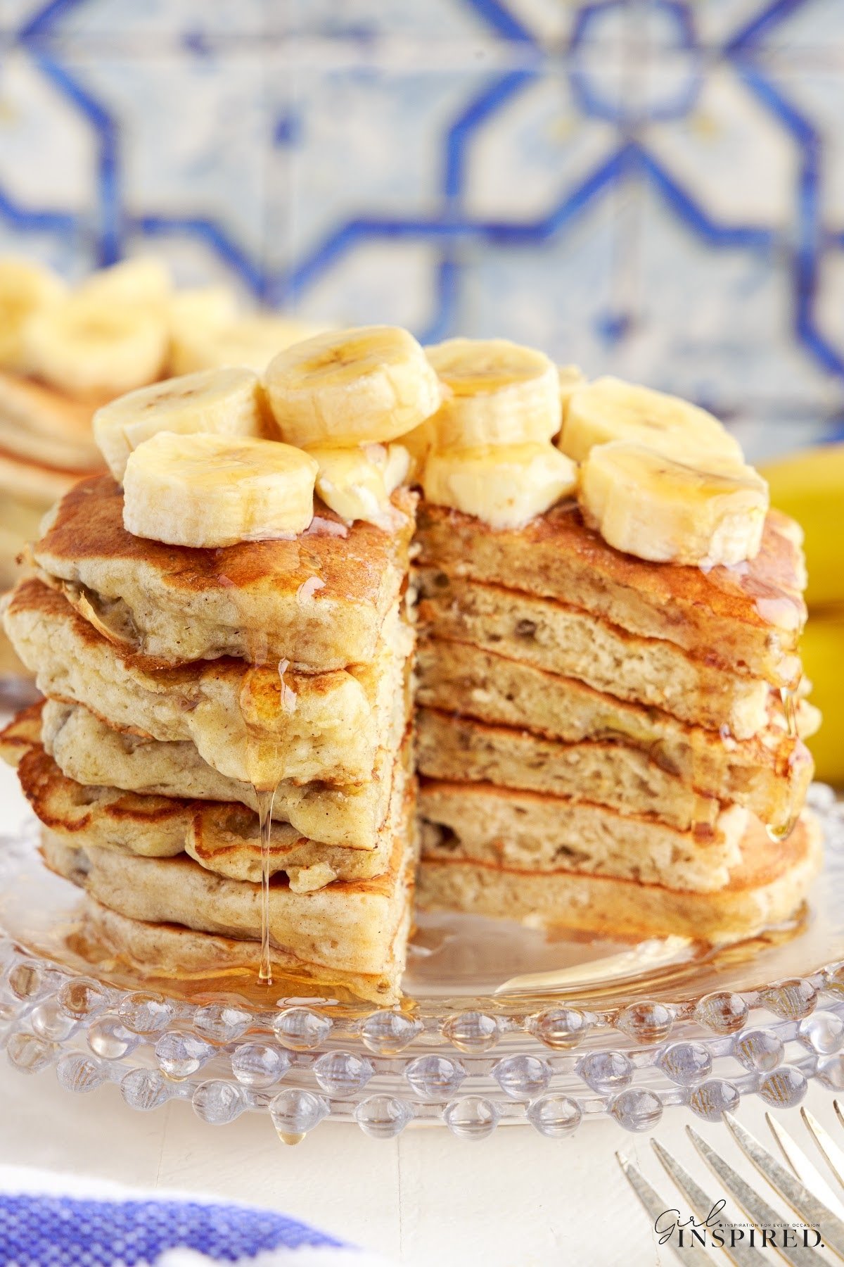 A stack of banana buttermilk pancakes topped with bananas with a slice taken from them.