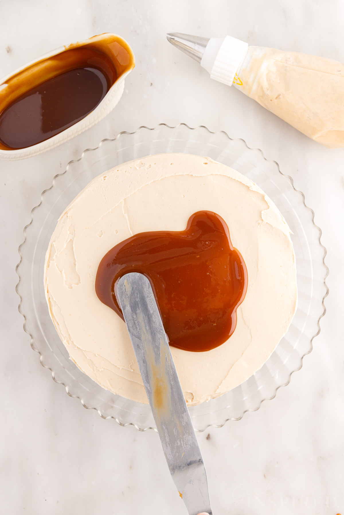 Icing spatula spreading a pool of caramel sauce over the top of the frosted salted caramel cake.