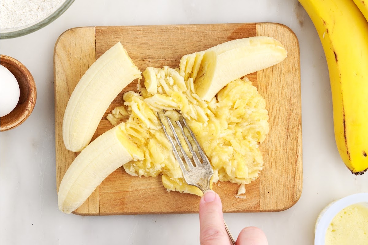Bananas on a cutting board, mashed with a fork.