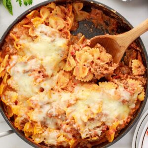 Overhead view of a skillet of Bow Tie Lasagna with a wooden spoon inserted.