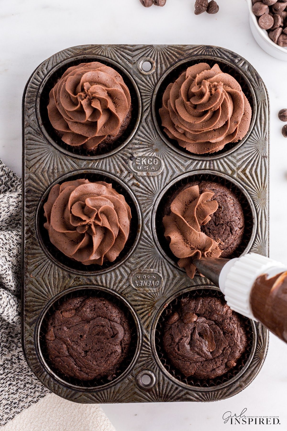 Six chocolate cupcakes being topped with Whipped Chocolate Ganache.