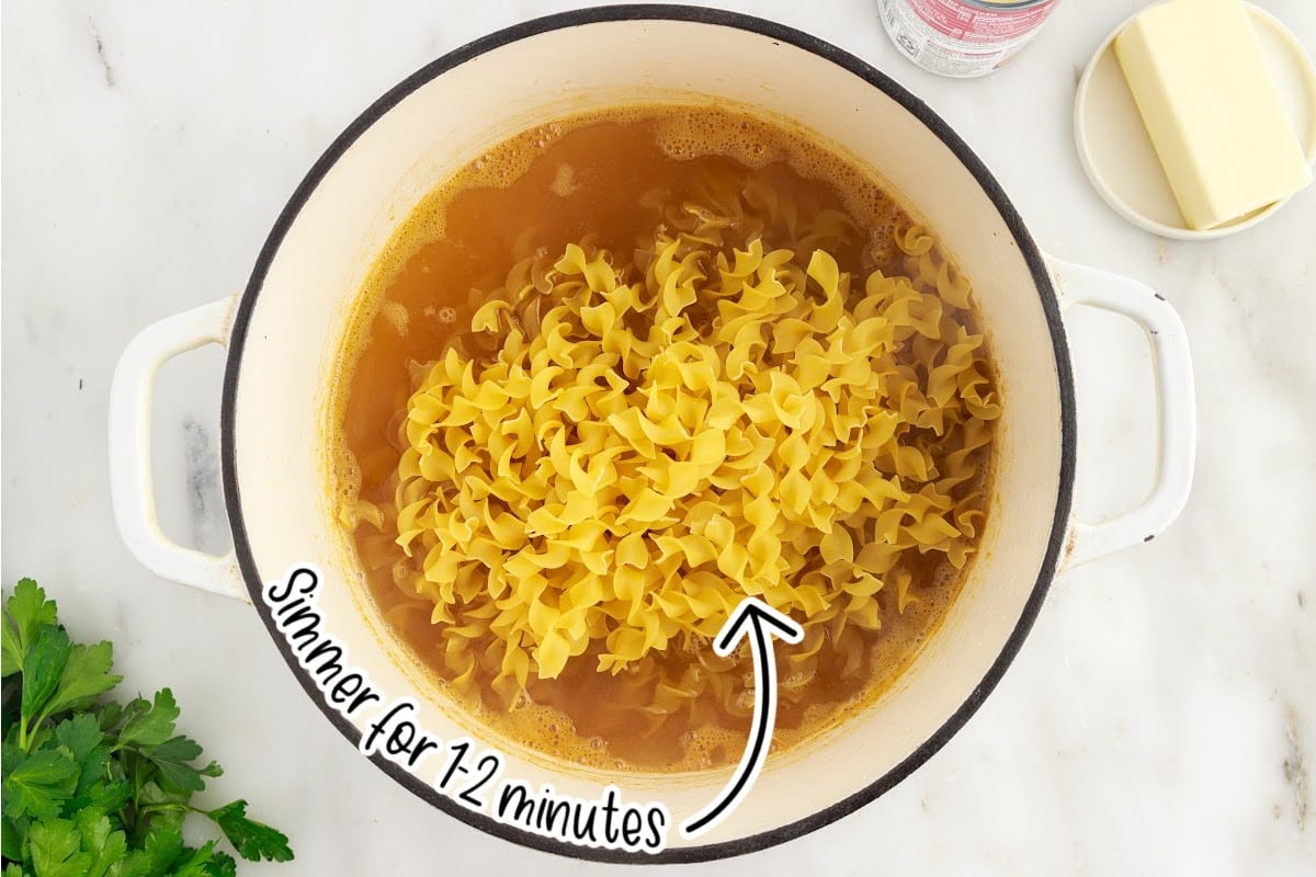 Noodles added to chicken broth in a dutch oven with text overlay.