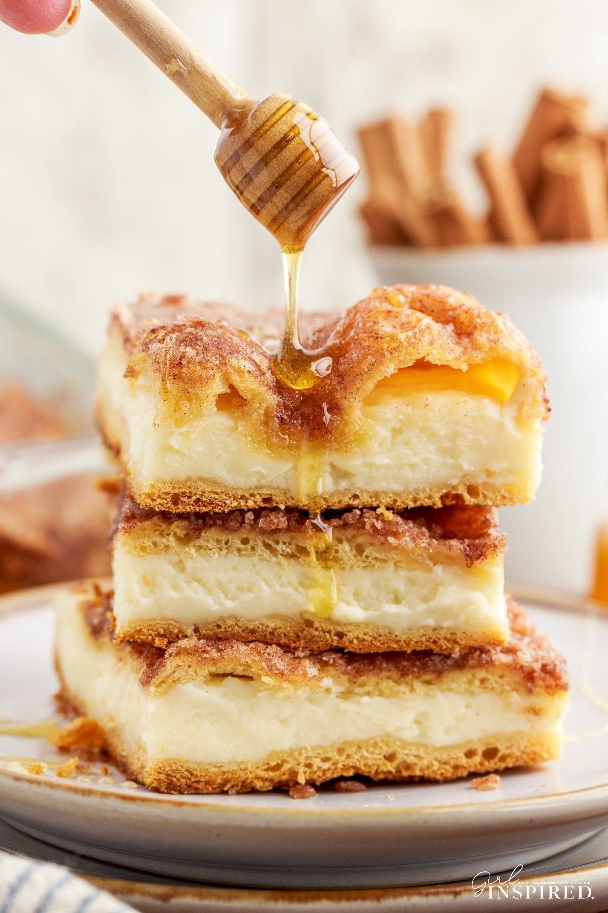 Three slices of Sopapilla Cheesecake stacked on each other drizzled with honey.