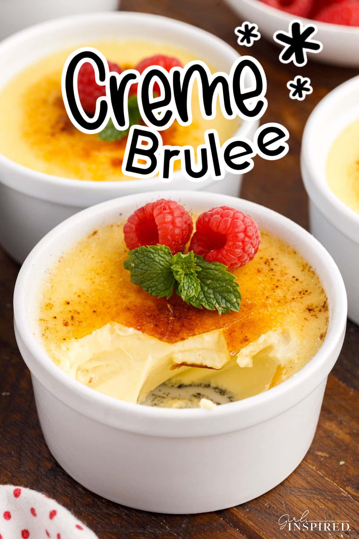 Vanilla Bean Creme Brulee in two ramekins with raspberries and mint leaves, with text overlay.