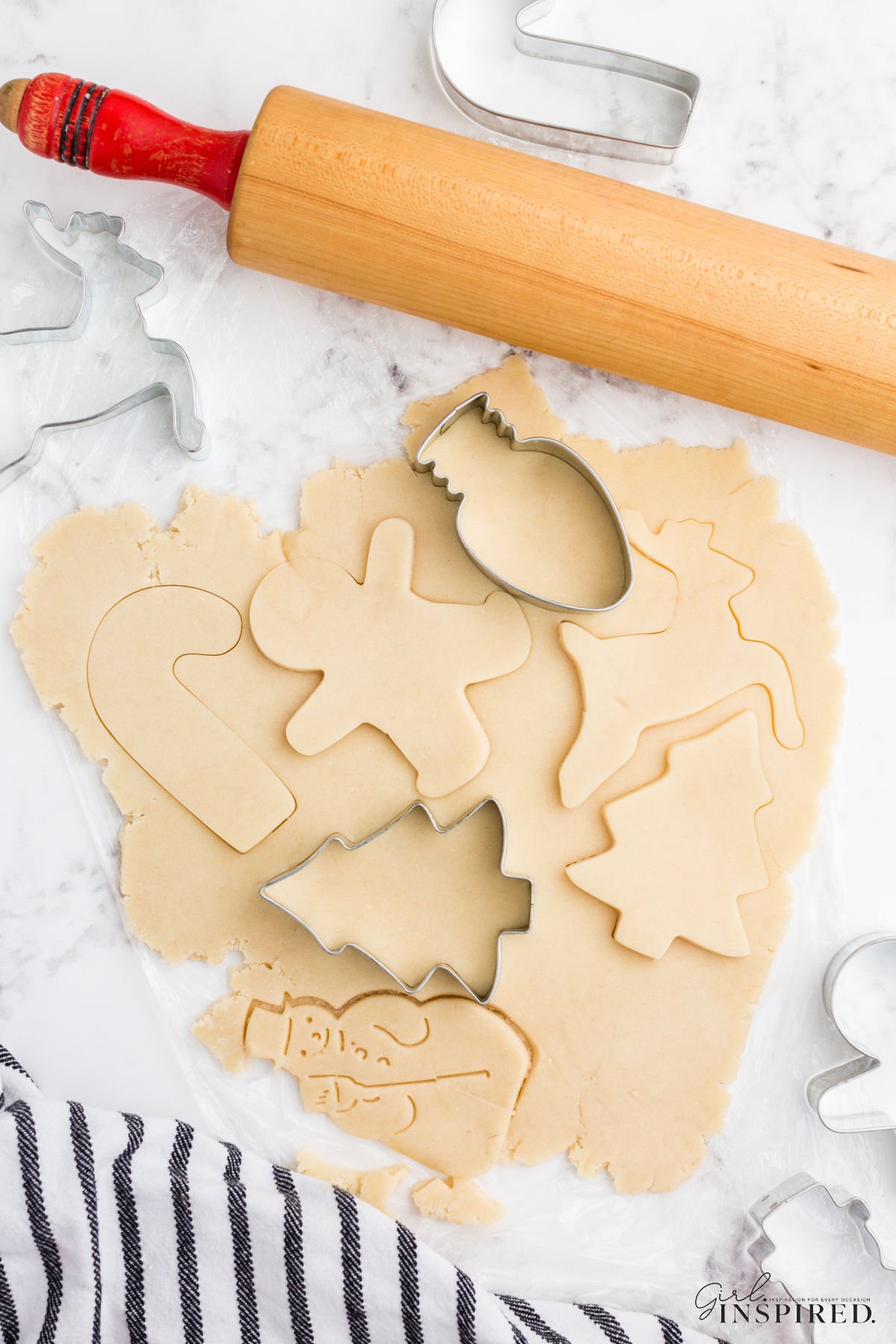 Cookie cutters on and around sheet of sugar cookie dough with various shapes cut into it.