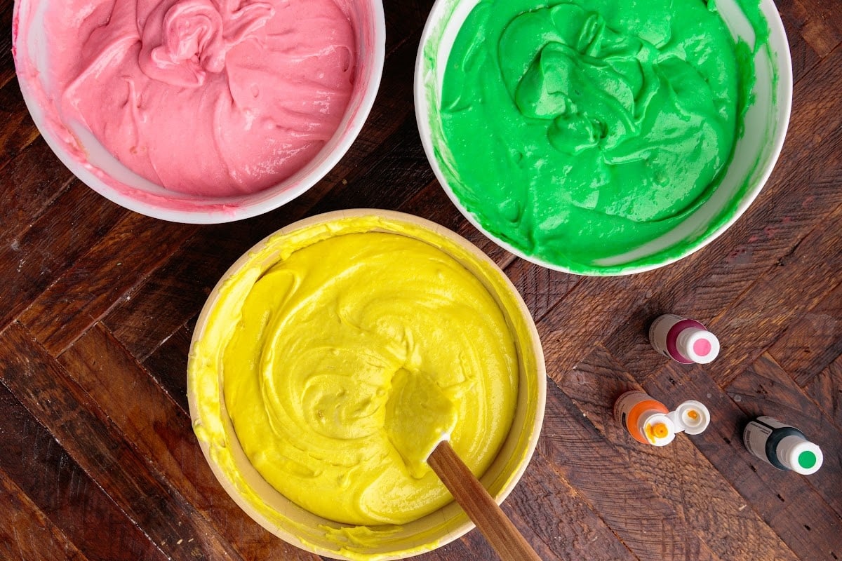 Italian Rainbow Cake batter colored pink, green, and yellow in three bowls.