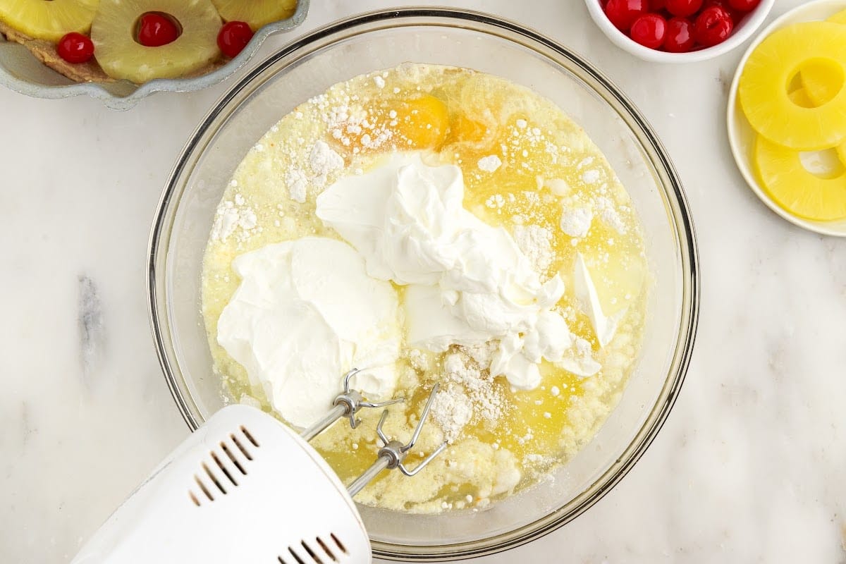 Cake mix, eggs, oil, pineapple juice, and sour cream in a mixing bowl.