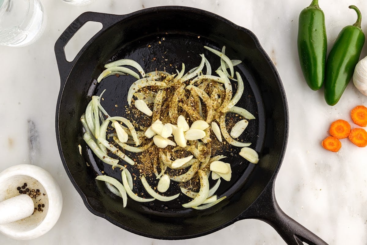 Garlic and seasonings added to cast iron skillet.