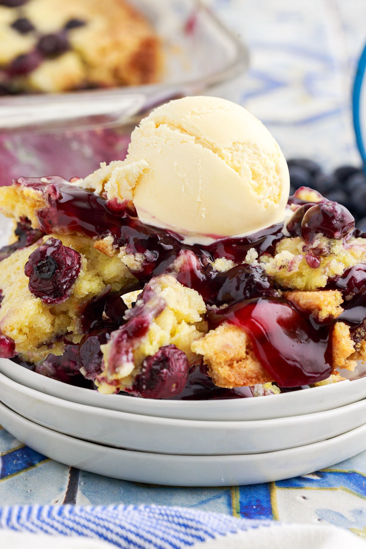 A scoop of ice cream on a serving of Blueberry Dump Cake on a dish.