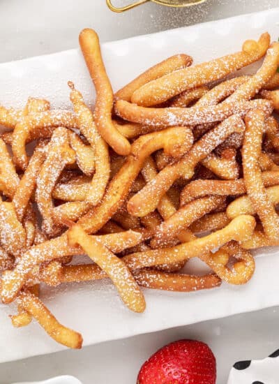 A platter of Funnel Cake Fries sprinkled with powdered sugar, with fresh strawberries as garnish.