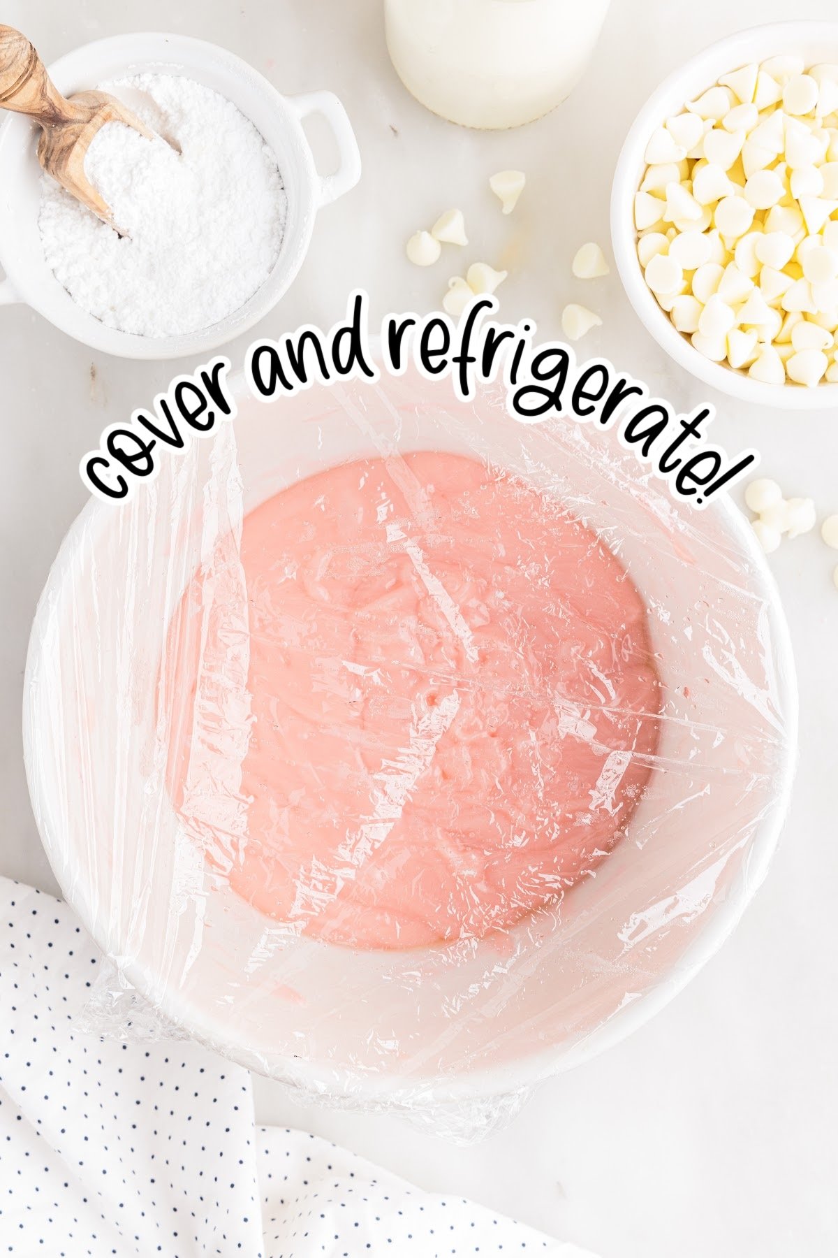 Plastic wrap covered bowl with pink strawberry truffle batter inside.