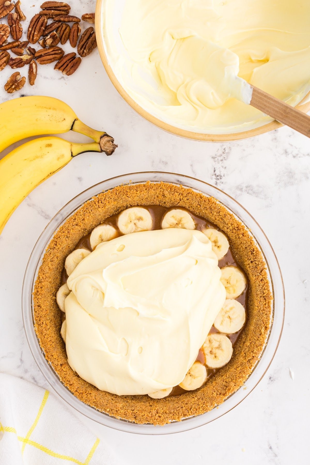 Layering the banana cream pie filling on top of sliced bananas and caramel in a graham cracker crust.