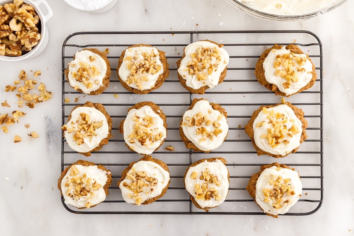 Cookies topped with crushed walnuts on top of the frosting, on a wire rack.