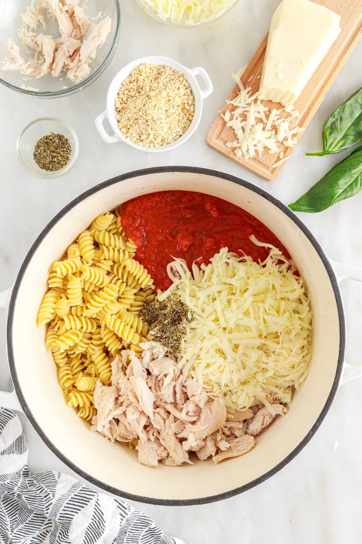 Noodles, chicken, cheese, sauce, and herbs in a large bowl.
