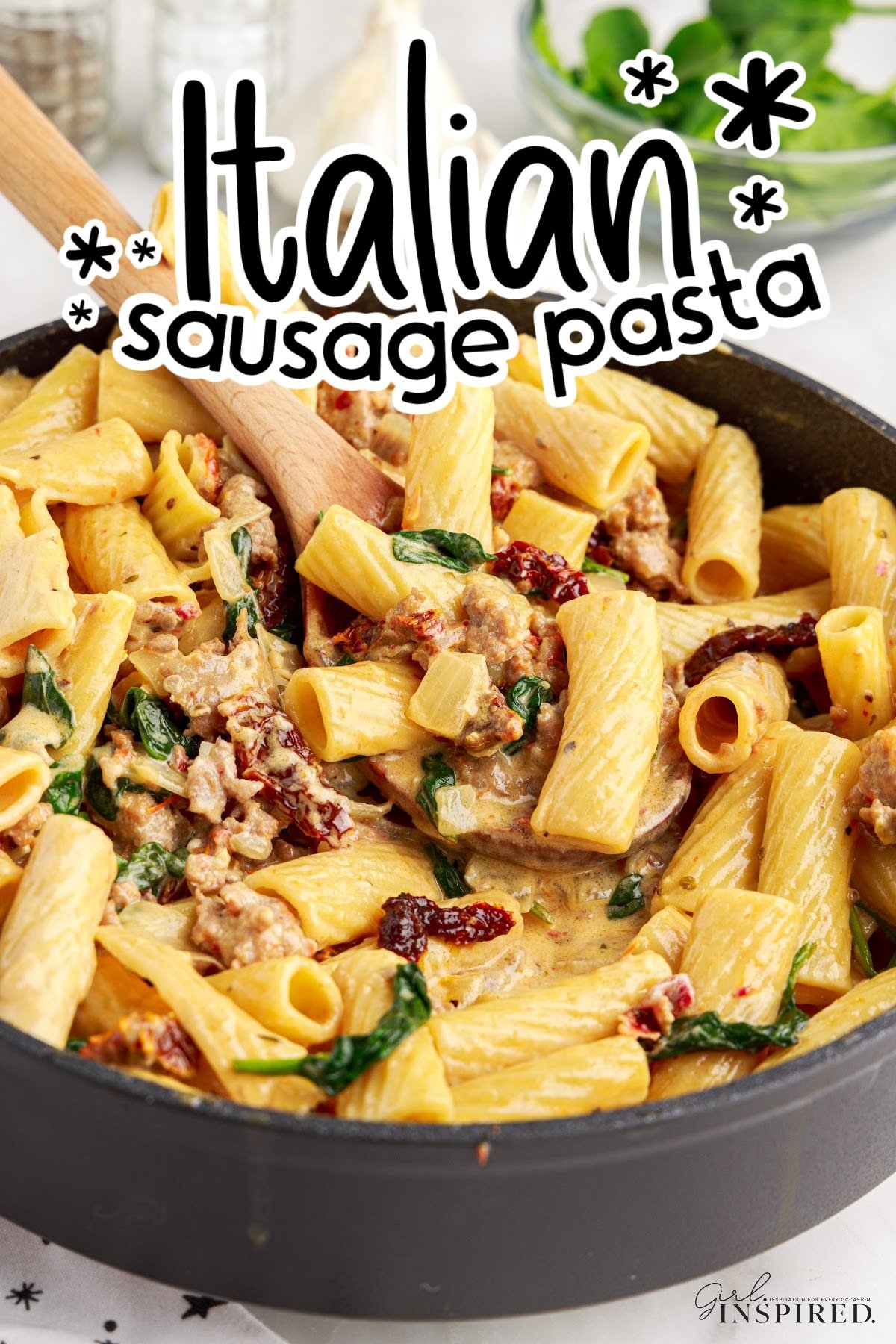 Italian sausage pasta in a large skillet with a wooden spoon, with text overlay.