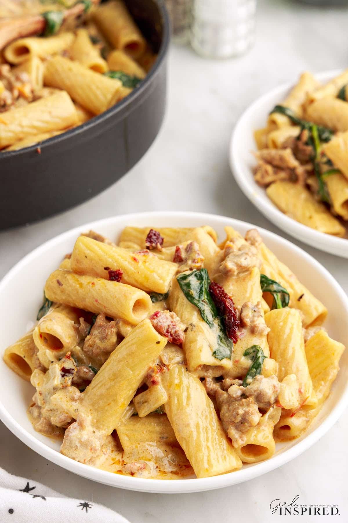 Two small plates of Italian sausage pasta next to the skillet.